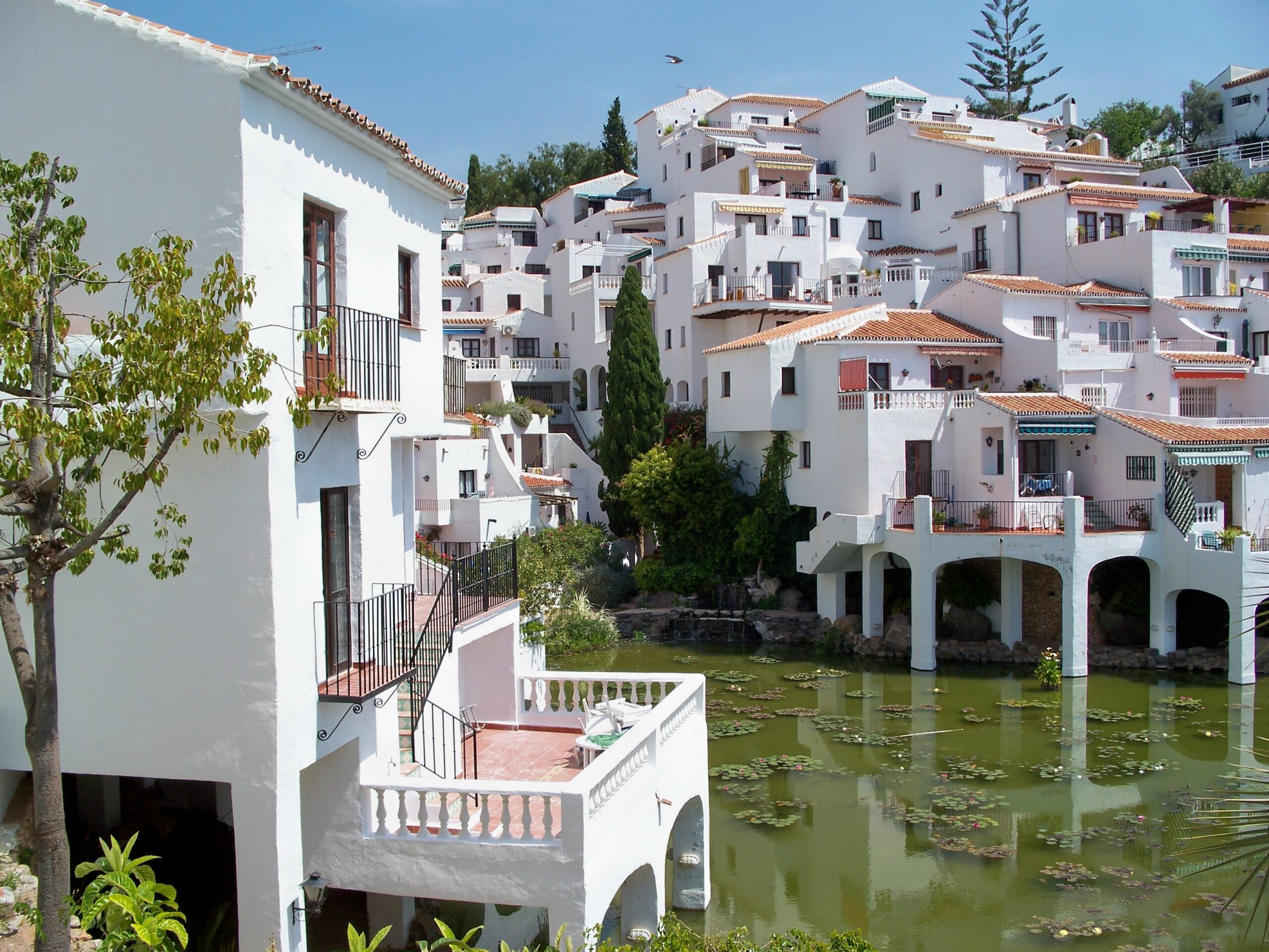 Viviendas blancas, vegetación y estanque en una zona común de una urbanización residencial de Nerja.